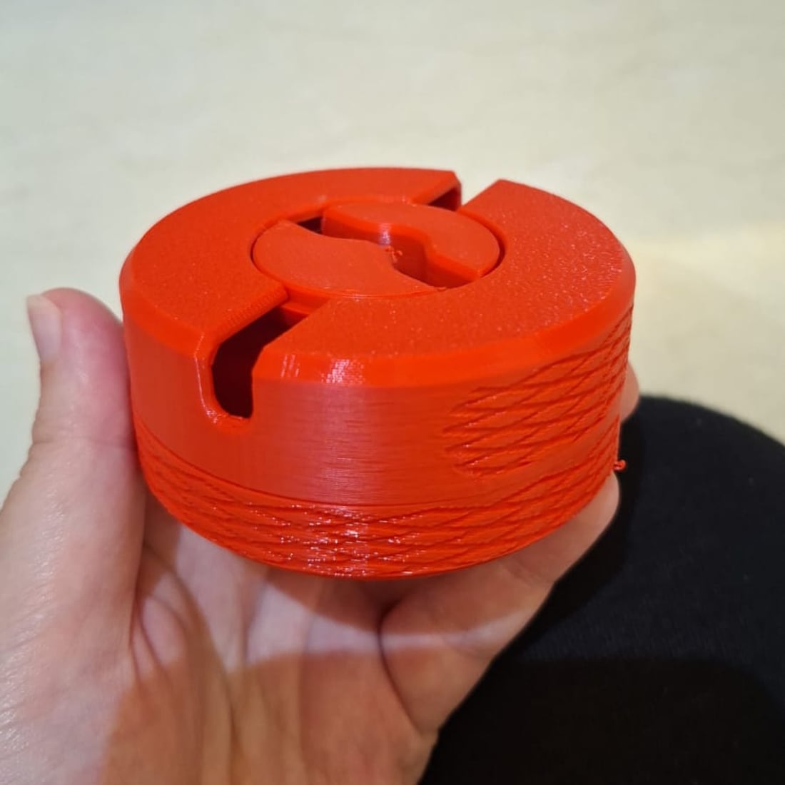 A black 3D-printed circular cable winder on a wooden desk with a braided microphone cable wound into it.