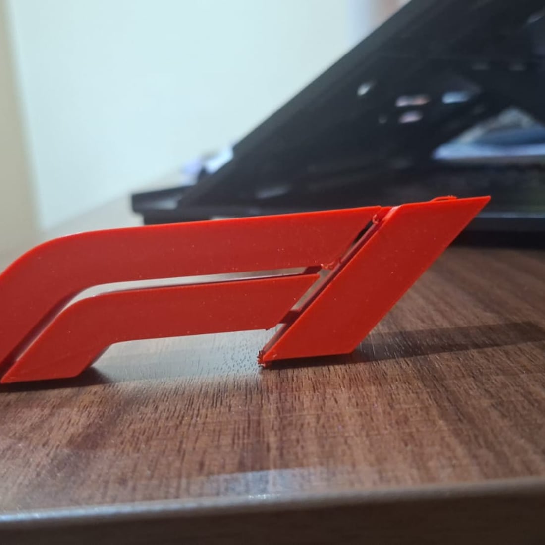 A red 3D-printed Formula 1 piece standing on a wooden desk.